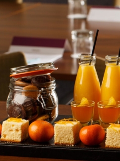 Selection of cakes, sweets and small bottles of orange juice lined up for a meeting at Mercure Hotels