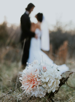 Bouquet in foreground with newlywed couple embracing in out of focus background