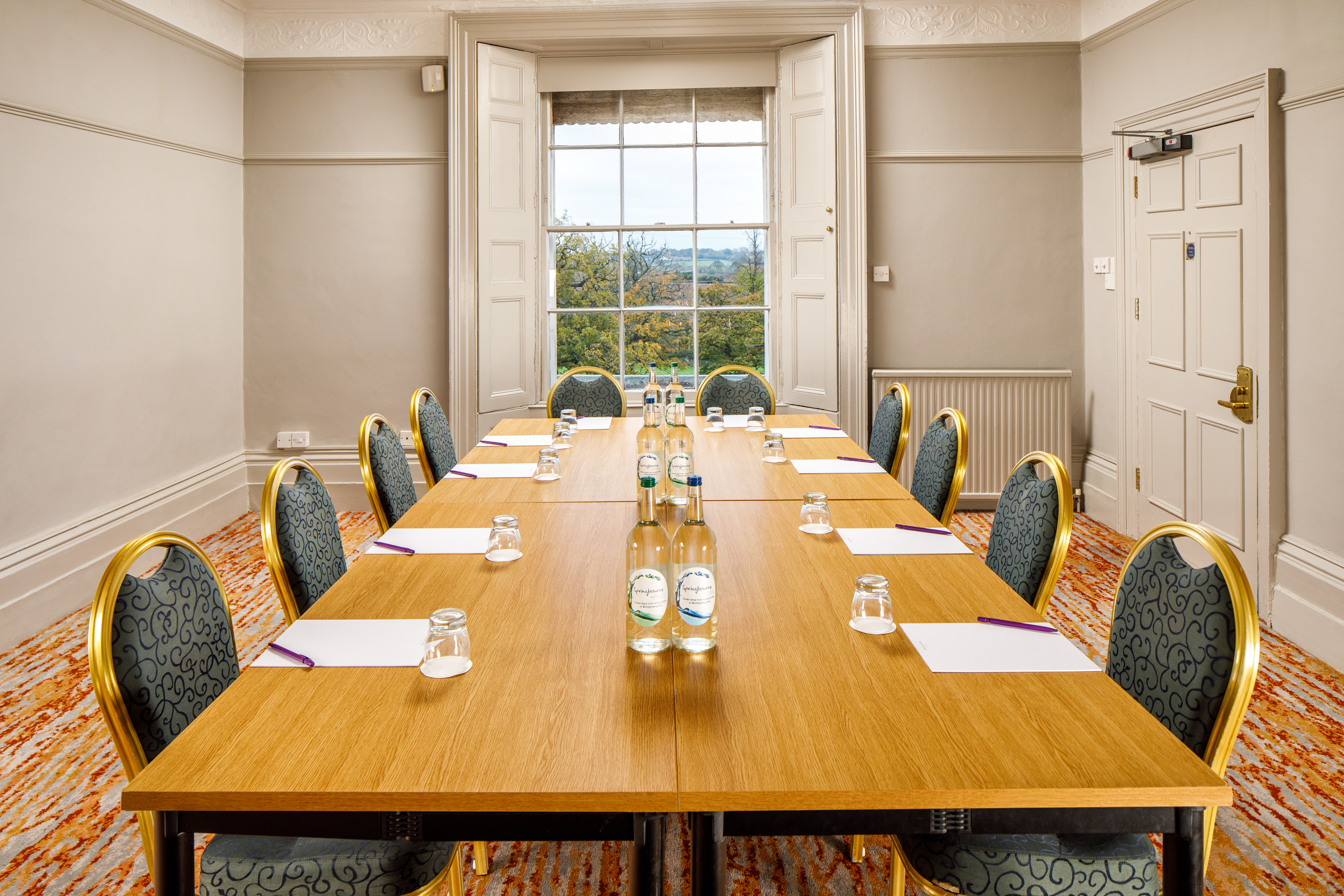 The long table seating 10 in The Boardroom at mercure gloucester bowden hall hotel ready for a meeting, with notepads and bottles of water on the table